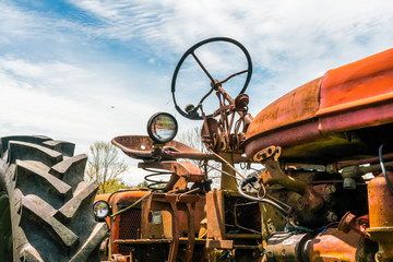 Close-up of old rusty farm tractor, low angle up towards plane in cloudy sky