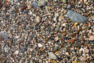 Thin white foam and the many small bubbles on the glittering sea water with the colorful pebbles underneath