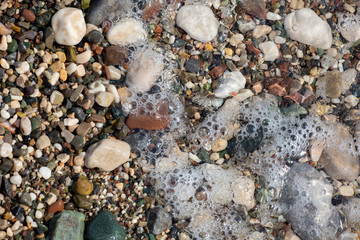 Thin white foam and the many small bubbles on the glittering sea water with the colorful pebbles underneath