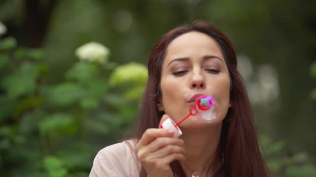 happy woman blowing soap bubbles in park
