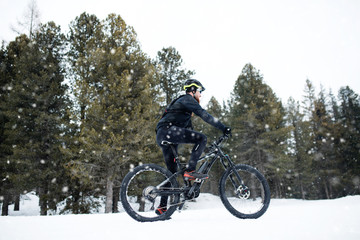 Fototapeta na wymiar Side view of mountain biker riding in snow outdoors in winter nature.