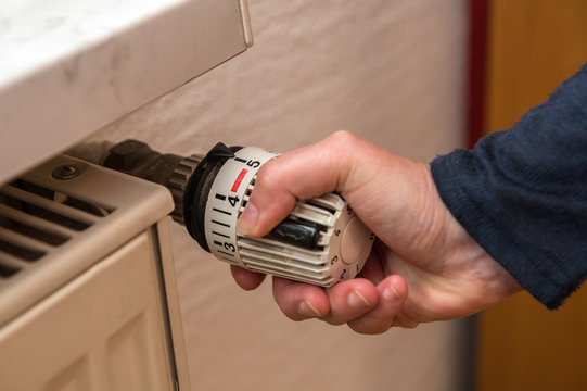 A woman has set a thermostat on a heater to a high value and wastes a lot of energy. Concept: heat or heating costs