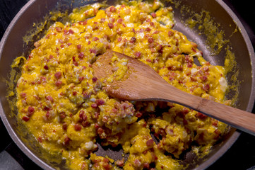 Scrambled eggs and bacon are cooked in a frying pan. Concept: cholesterol or food
