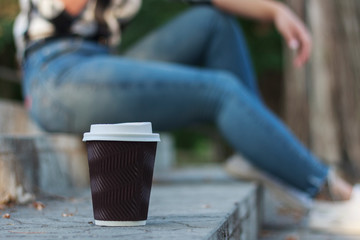 paper cup with coffee on the steps, against the background of a girl who is talking on the phone