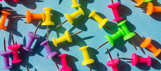 Creative school flat lay top view.Set of push pins of different colors on a blue background with shadows and hard light, school art background