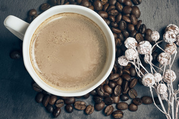 Top view of hot coffee in a white cup with roasted coffee beans and autumn decoration on slate background