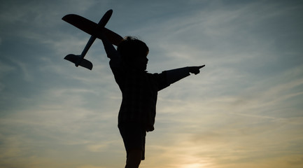 Child aviator with airplane dreams of traveling in summer in nature at sunset. Boy with plane on meadow. Summer leisure. Child care.