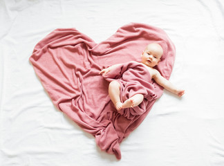 Smiling baby lying on a pink blanket in the shape of a heart