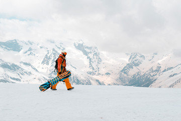 man snowboarder with a snowboard in his hand is on the snow in the mountains