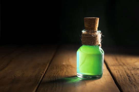Potion in magic bottle on black and wooden background. Copy space. Selective focus