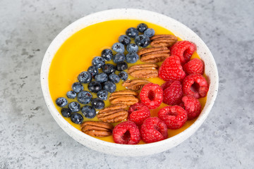 Vegetarian health food. Mango and orange smoothie bowl with fresh berries and nuts.