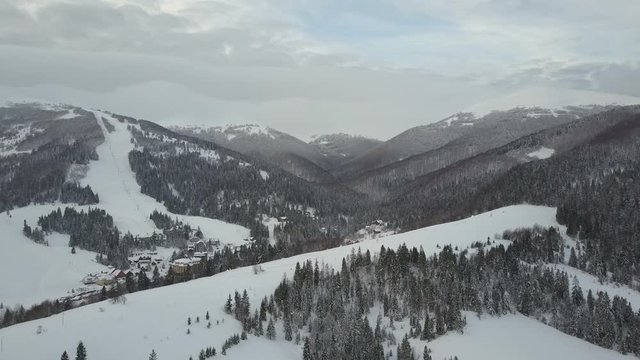 Flight over a village in Carpathian mountains and a ski resort next to it. Bird's eye view of snow-covered houses in mountains. Rural landscape in winter. Carpathian village in the snow from a height.