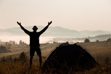 Silhouette of man raised his hands with the backpack on camping holidays at sunset on top of mountains