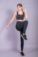 Young slim girl is jumping on a gray background. Photo of an active woman in sportswear.