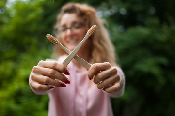 Young beautiful girl holds a useful bamboo toothbrushes and smiles looking at the camera. Environmental friendliness and zero waste concept.