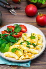 Slices of zucchini baked in spices with cheese on a plate with tomatoes and arugula on a wooden table. Close-up
