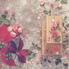 Withered roses are in a vase on a wooden box. Nearby are scattered dried flowers and leaves. Autumn composition. Flat lay.