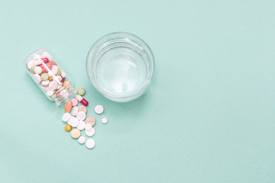 Creative Flat Lay Overhead Of Colorful Drugs In A Glass Bottle And Glass Of Water On Light Green Background. Seasonal Diseases And Health Care Concept. Template Medical  Blog Social Media.