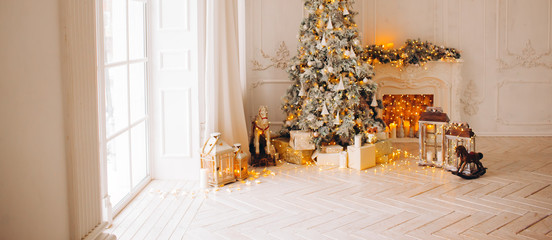 classical interior of a white room with a decorated fireplace, luxury Christmas tree, garlands, candles, lanterns, gifts. day. pink sofa pastel colors