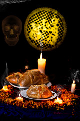 Pan de muerto traditional recipe from Mexico, adorned with candles and cempasuchil flower petals, in the background chopped papael and candle commemorating the Day of the Dead