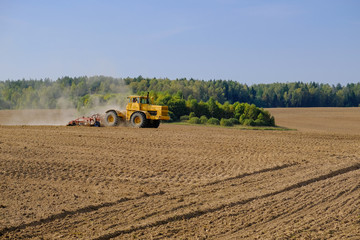 A farm tractor cultivates land after harvesting grain.