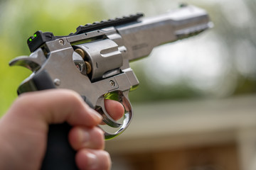 in one hand is large silver heavy revolver and aims into the air