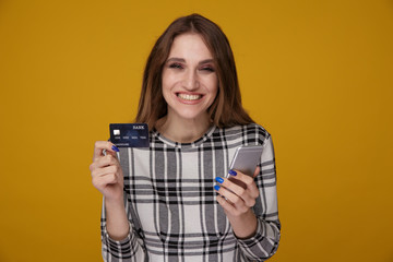 Fototapeta premium Young woman with phone and credit card standing isolated in the studio