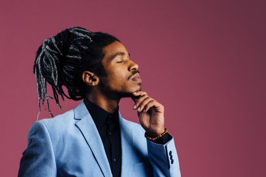 Portrait of a man with cool hair and eyes closed, against studio background