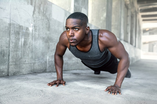 Black male working out alone outside on concrete, pushups in urban downtown city exercise