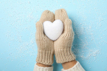 Girl holding in hands white heart on blue background with snow, space for text