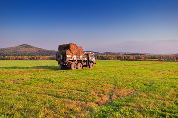 The truck carries rolls of hay against the background of the forest and mountains. After the harvest. Early autumn.