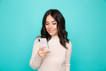 Beautiful curly hair female holding cellphone standing on the blue background