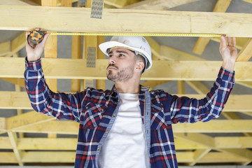 young male builder measuing beam