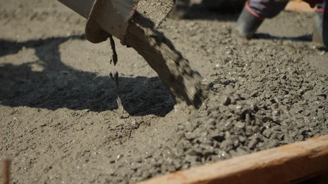 Close up shot of wet cement pouring out from cement truck shoot at a construction site as workers spread it out with shovels during afternoon.