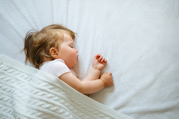 Cute little baby sleeping peacefully on bed at home covered with blanket. Child daytime sleeping schedule