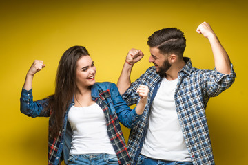 Obraz premium Young, cheerful people man and woman in basic clothing smiling and clenching fists like winners or happy people isolated over yellow background.