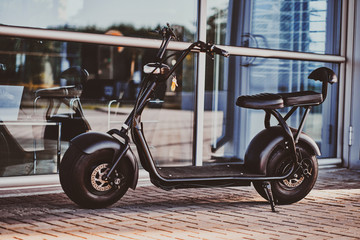 Trendy electrical scooter is parked near glass building at bright summer day. - obrazy, fototapety, plakaty