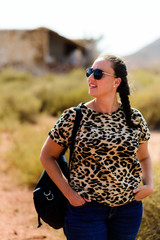 Portrait of smiling young woman wearing sunglasses and backpack walking through the field. nature concept
