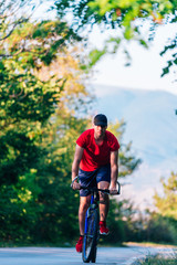 Obraz premium Fit cyclist rides his bicycle (bike) on an empty road in nature wearing a baseball hat and red t-shirt.