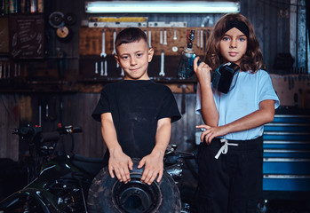 Fototapeta na wymiar Pretty little kids are holding weel and screwdriver while posing for photographer at auto service.