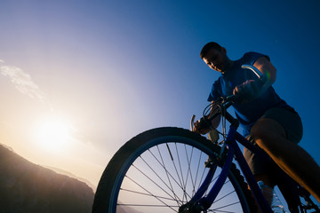 Naklejka na ściany i meble Close up silhouette of an athlete (mountain biker) riding his bike on rocky mountains.