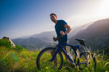 Perspective of a fit mountain biker pushing his bike uphill with amazing view on a forest, river...