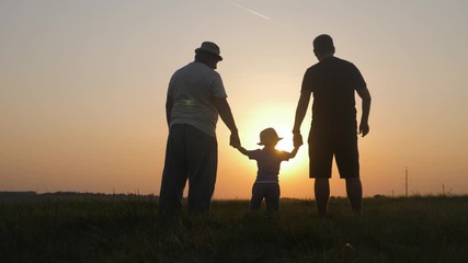 Small boy with father and grandfather at sunset, silhouette concept. Three generations of a family.