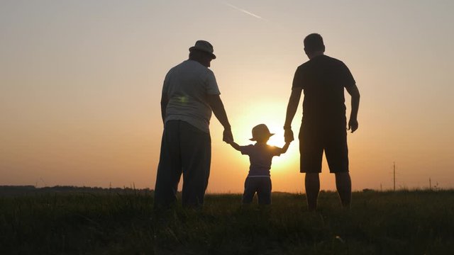 Small boy with father and grandfather at sunset, silhouette concept. Three generations of a family.
