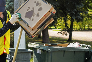 a janitor puts empty pizza boxes in a dumpster.