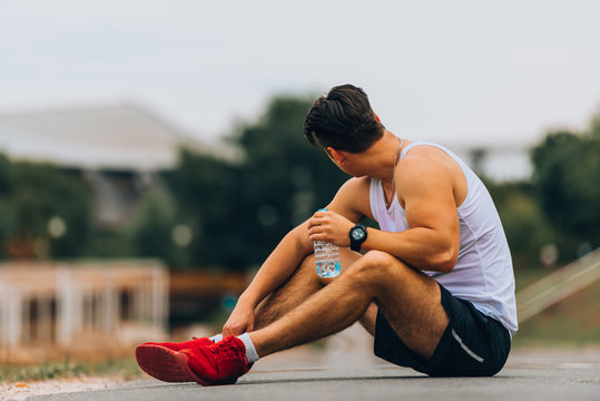 Tired Male Runner Holding Waterbottle While Sitting On Ground