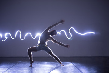 Modern Dance performer dancing with a neon blue light while making gracious moves and spectacular body art expressions.
