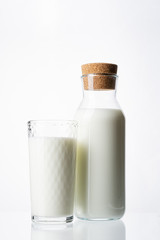 A glass filled with milk and a bottle with milk on a white background.. Glass bottle. Natural cork. White drink. Cow's milk.