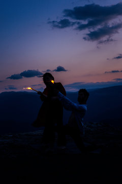 Happy romantic couple dancing open air under sunset sky with fire sticks, low key, dark image
