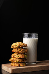 Glass with milk on a wooden board. Homemade cookies. Black background. White drink. Cow's milk. Pyramid of cookies. Cookies on top of each other.